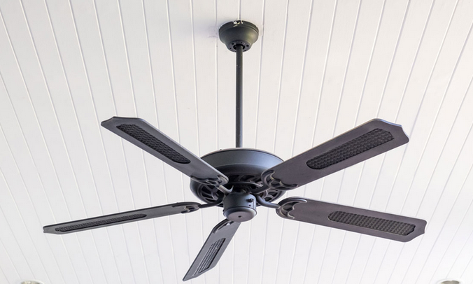 This image shows a black ceiling fan with five blades mounted on a white wooden plank ceiling.