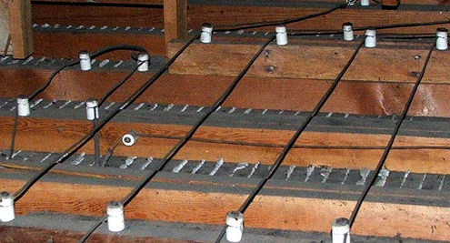 This image shows wooden floor joists or beams in a construction framework with white mounting brackets or hangers attached at regular intervals.